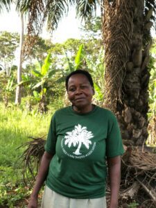 Rose Kembabazi, eine lokale Farmerin, in der Nähe ihrer Ölpalme, ein stolzes Mitglied der Parrot Tree Caretakers Association. © PTCA