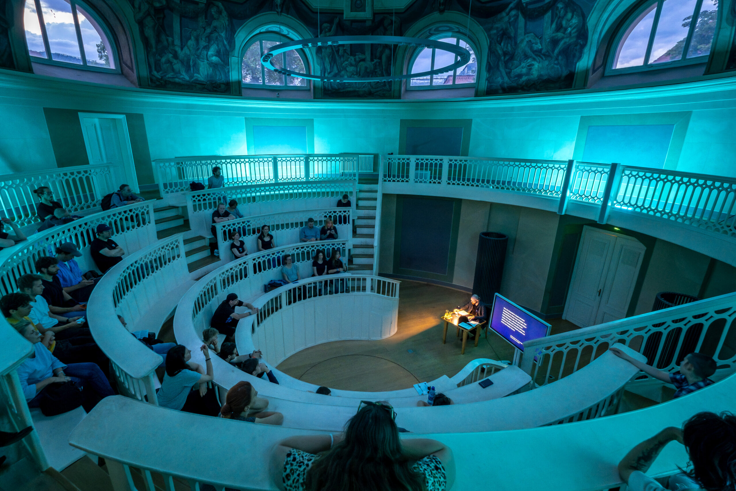Blaues Licht erfüllt den historischen Hörsaal im Tieranatomischen Theater und erzeugt die Atmosphäre eines Tauchgangs. Das Publikum sitzt auf den geschwungenen Rängen und lauscht Texten und Klängen über die Tiefsee.