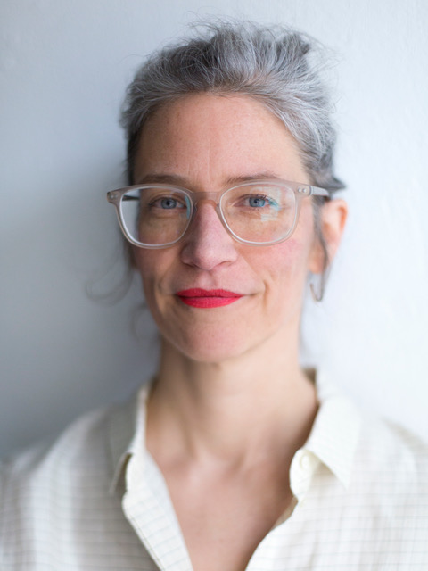 Porträt der Autorin Evke Rulffes. Sie blickt direkt in die Kamera und trägt eine große, transparente Brille, rote Lippen und ein weißes Hemd. Ihr graues Haar ist nach hinten gebunden. Im Hintergrund ist eine helle, weiße Wand zu sehen. Die Aufnahme ist als Nahporträt gestaltet und zeigt vor allem Gesicht und Oberkörper. Foto: Jasper Kettner.